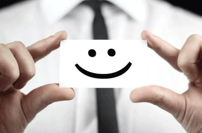 Person in a white shirt and tie holding up a card with a smiley face