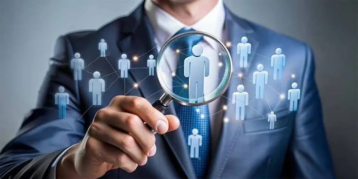 Person in a suit holding a magnifying glass over a network of people icons