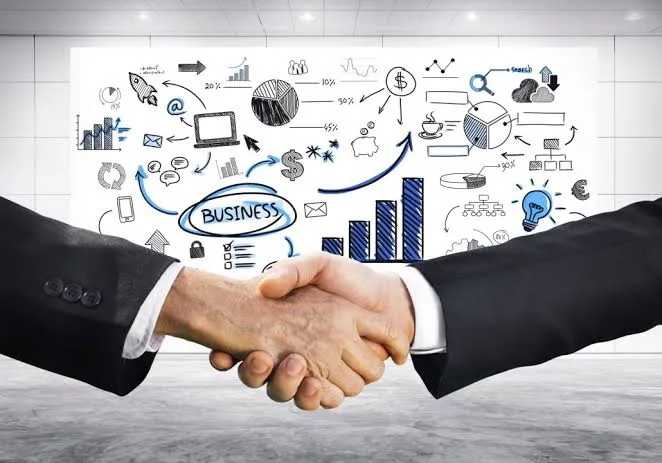 Two business people shaking hands in front of a whiteboard of charts and business sketches